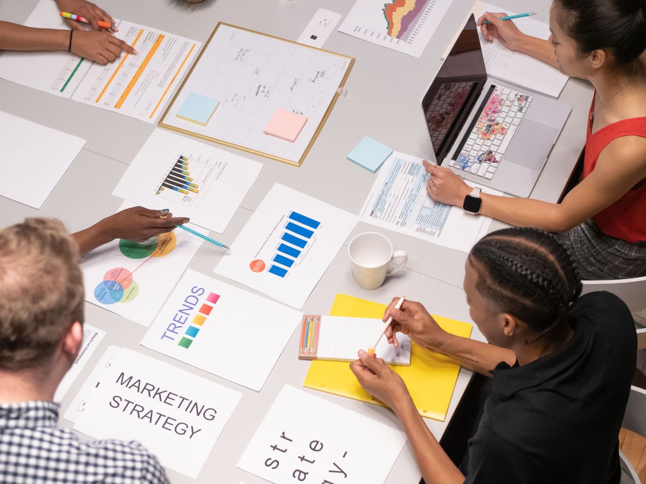 Vue de dessus d’une équipe diversifiée analysant des stratégies marketing à l’aide de graphiques et de tableaux.
